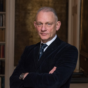 A man with short grey hair wearing a dark suit and tie