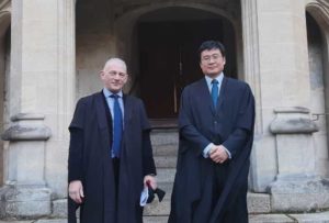 Photo of two men in black academic gowns and suits standing on stone steps