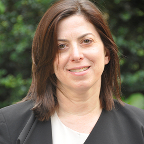 Woman with shoulder length dark brown hair wearing a white blouse and dark jacket