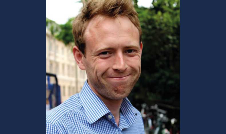 photo of a man with short light brown hair wearing a blue shirt