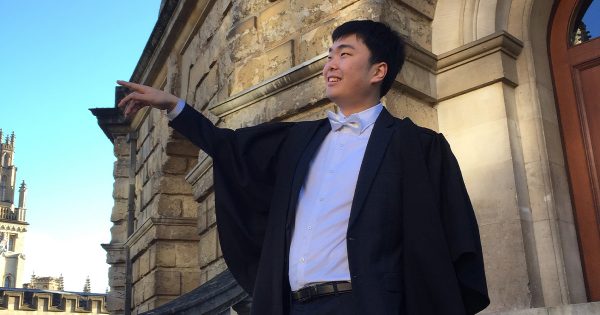 A man with short black hair wearing academic dress standing on the steps of the Radcliffe Camera in Oxford