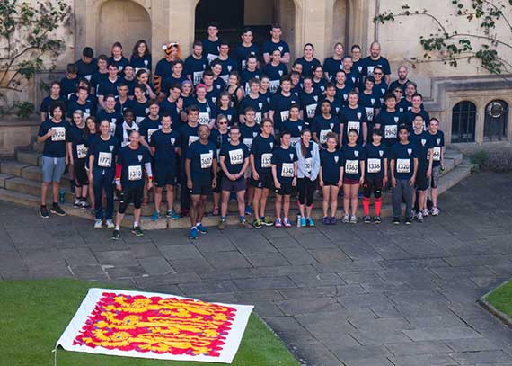 People in running clothes gathered on the steps of Oriel College with a flag depicting three lions