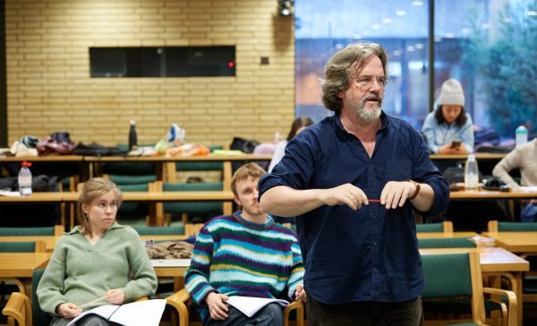 Imogen Usherwood-Bliss sitting with her fellow assistant director in the background and Sir Gregory Doran directs in the foreground