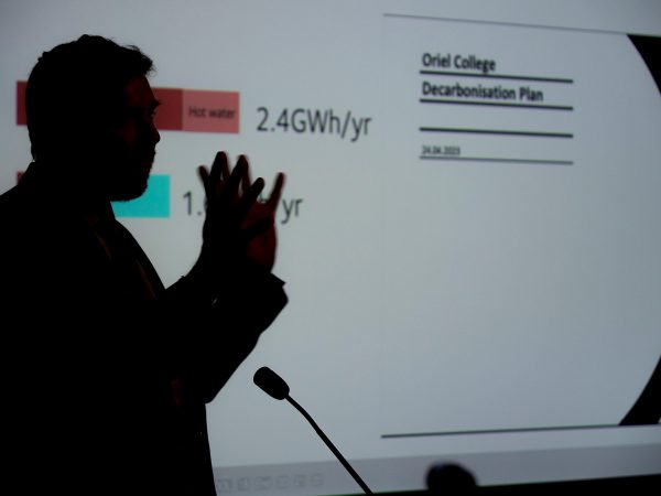 Dr Phil Grünewald with a screen in the background with text that reads "Oriel College Decarbonisation Plan"