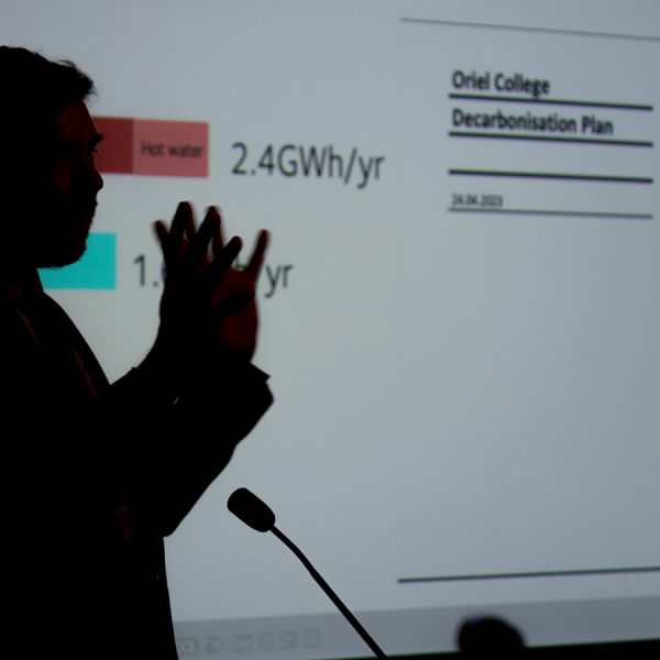 Dr Phil Grünewald with a screen in the background with text that reads "Oriel College Decarbonisation Plan"