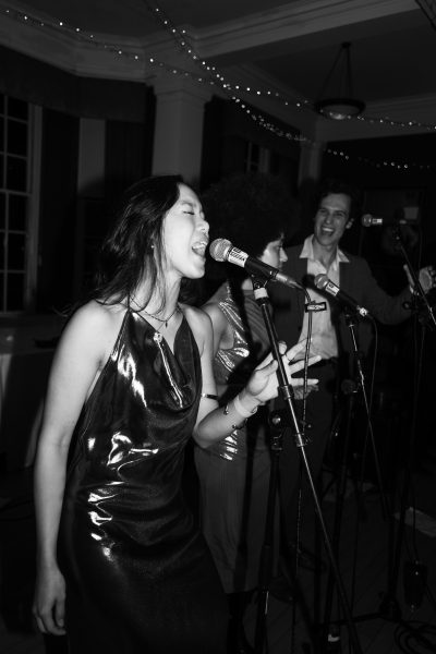 A young woman wearing black singing into a microphone on stage