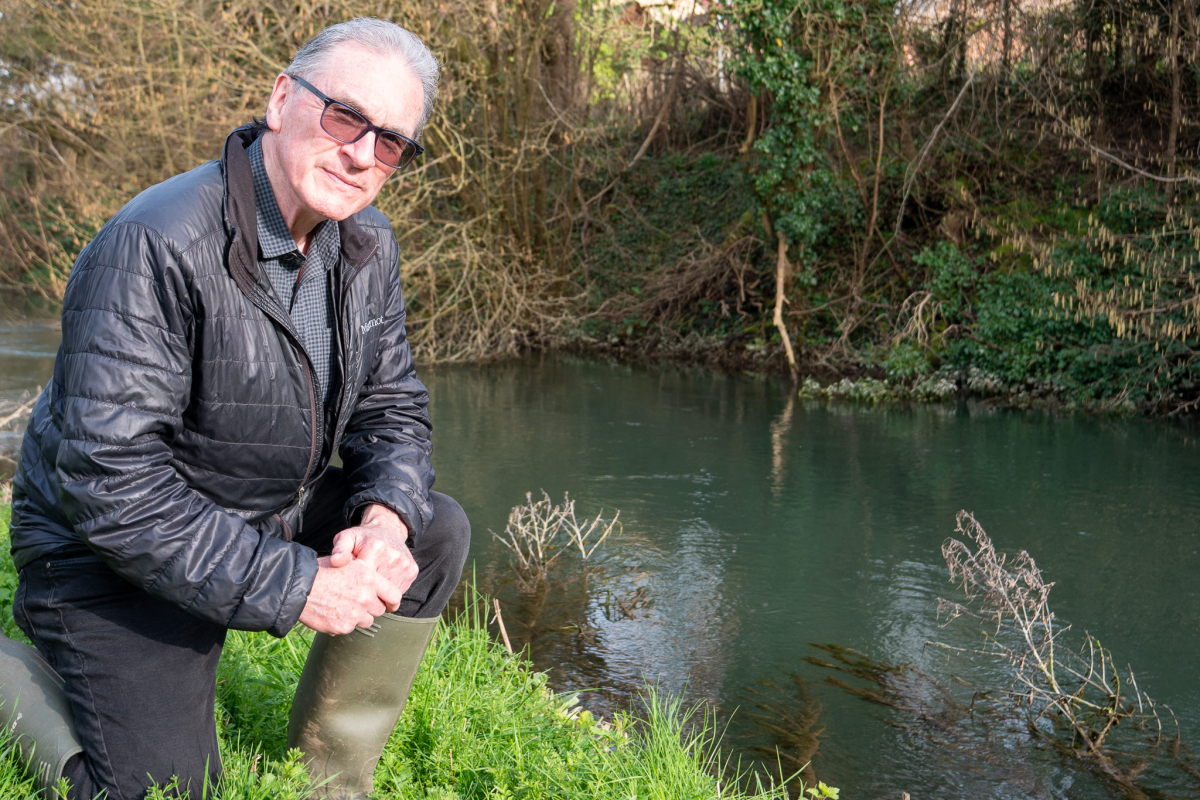 Peter Hammond knelt down at the side of the River Windrush.